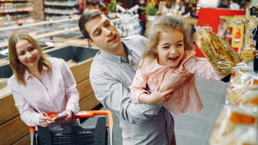Joyful family of three enjoying grocery shopping together in a supermarket.